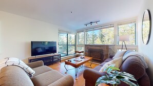 Ein Wohnzimmer mit Fernseher, Kamin und großen Fenstern.