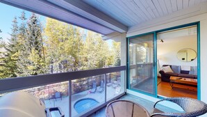 Ein Balkon mit Glastür, der zu einem Wohnbereich, einem Pool und Sitzgelegenheiten im Freien führt.