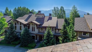 Un quartier résidentiel composé de plusieurs maisons, chacune présentant un style architectural distinct et étant entourée d’une végétation luxuriante, avec des montagnes en toile de fond.