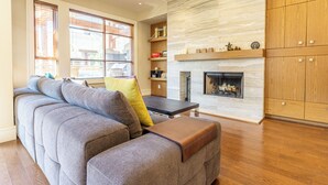 Un salon moderne avec un canapé d’angle, une cheminée et des meubles de rangement en bois.