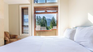 Une chambre à coucher avec un grand lit, un fauteuil à motifs léopard et une vue sur les arbres et les montagnes, visible par la fenêtre.