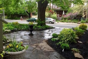 Uma rua residencial com caminho de pedra, vegetação exuberante e casas.