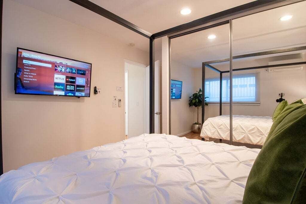 A modern hotel room with a large bed, a flat-screen TV mounted on the wall, and a sliding door leading to a bathroom.