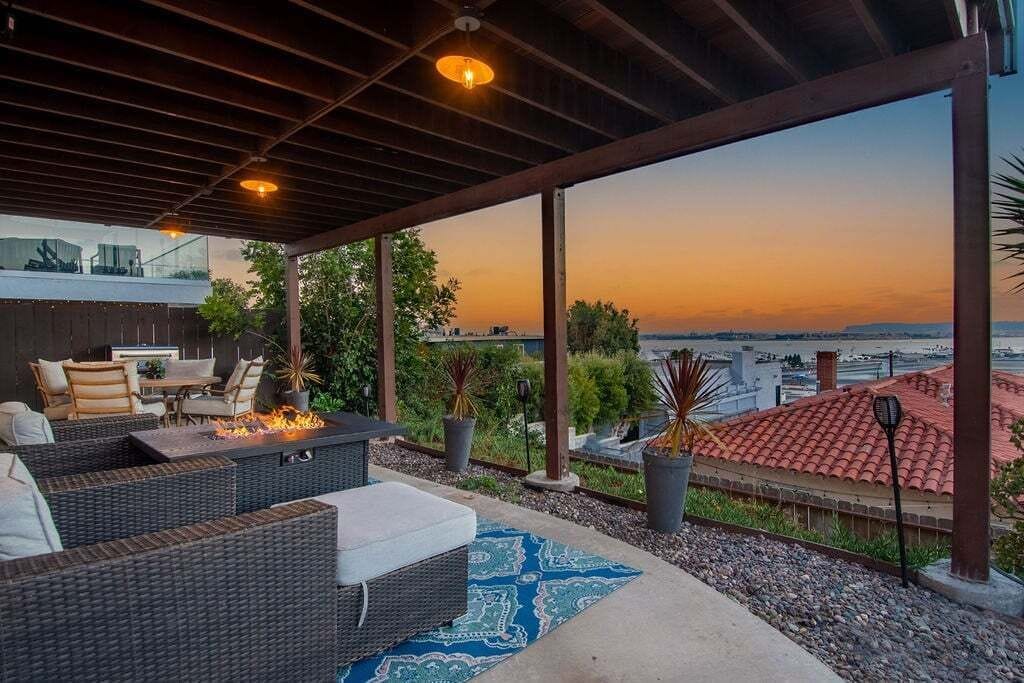 Un patio exterior con mobiliario de mimbre, una chimenea y vistas a la ciudad al atardecer.