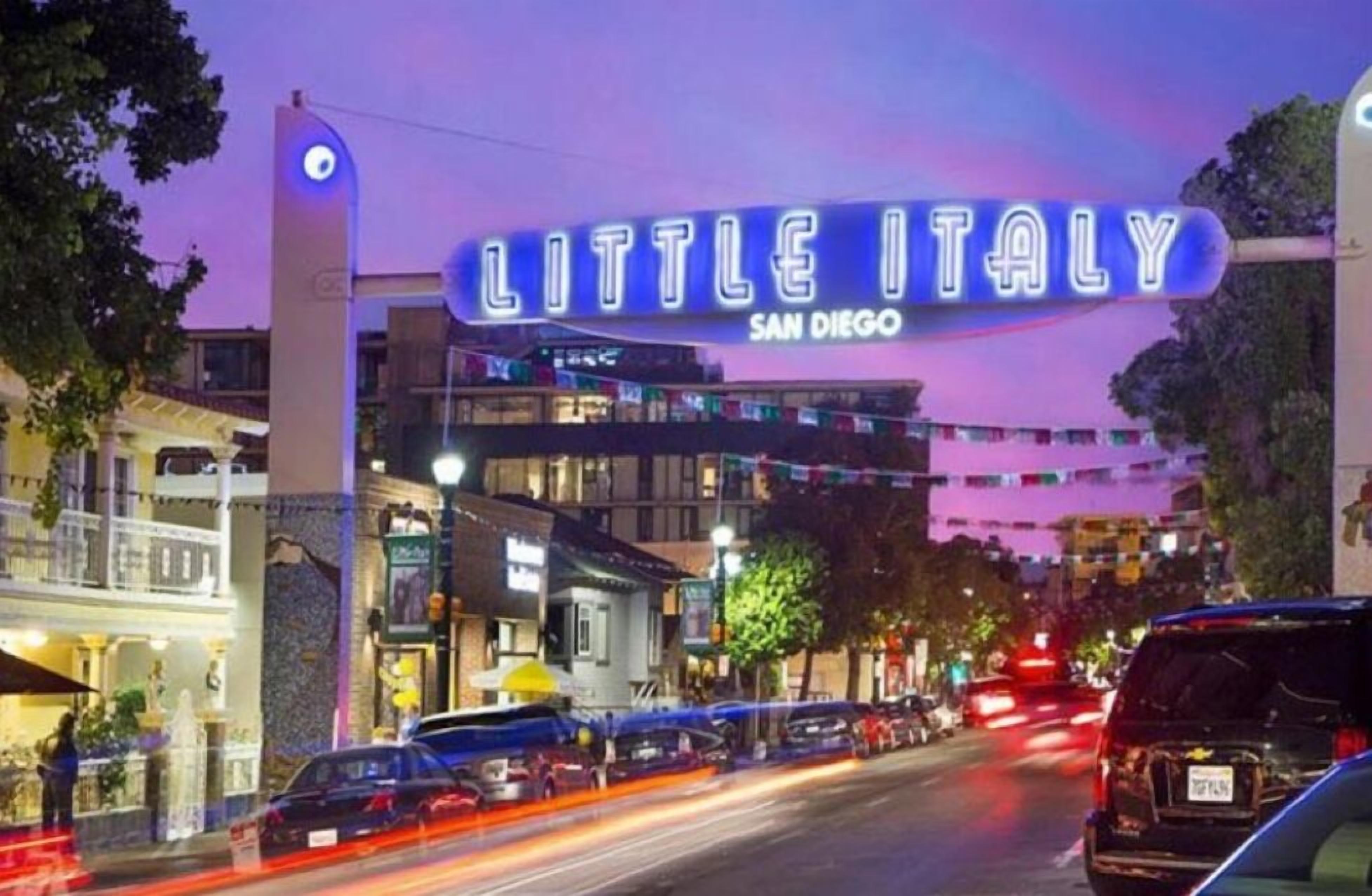 A street view of Little Italy in San Diego with a neon sign, cars, and buildings.