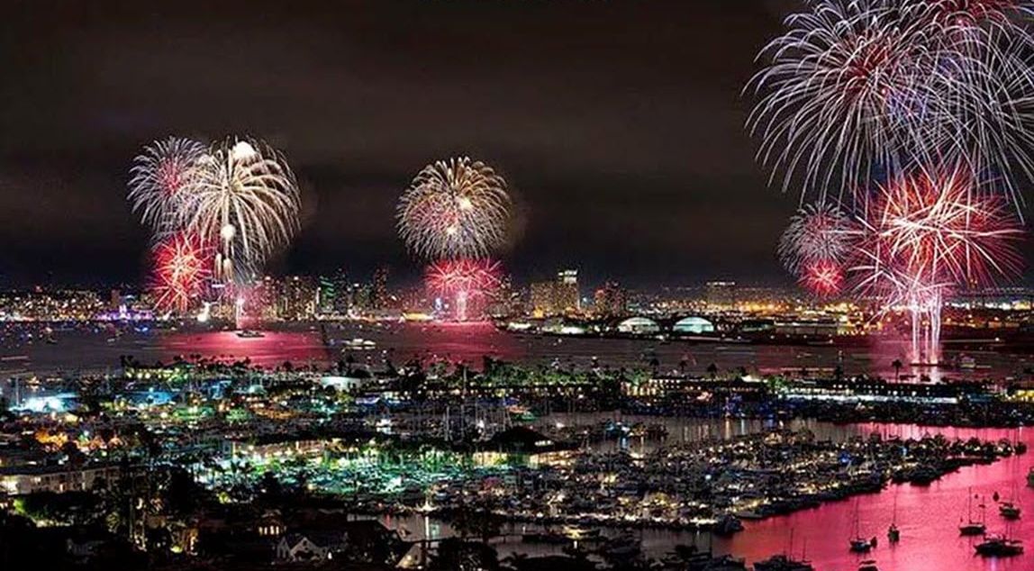 A nighttime cityscape with fireworks over the bay, indicating a festive atmosphere.