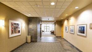 A hotel hallway with patterned carpet, framed artwork on the walls, and a trash can.