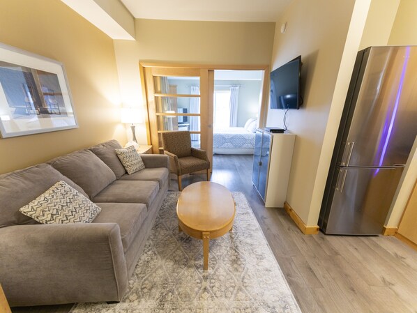 A modern living room with a sofa, armchair, coffee table, and a TV mounted on the wall. - Gimli Beach Condos # 2 - Gimli's best location! (Gimli)