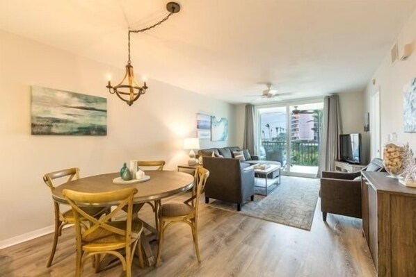 Un salon moderne avec un coin repas, agrémenté d’un lustre, d’un parquet en bois et d’une grande fenêtre offrant une vue dégagée.