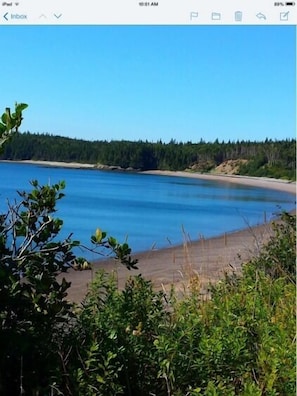 A beach with clear blue water, a sandy shore, and dense forest in the background. - Seaside Cottage On Beautiful New Brunswick Beach<br> (Seeleys Cove)