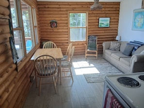 LâintĂ©rieur dâune cabane en rondins, avec une table Ă manger, des chaises, un canapĂ©, une cheminĂ©e et des Ćuvres dâart accrochĂ©es aux murs.
