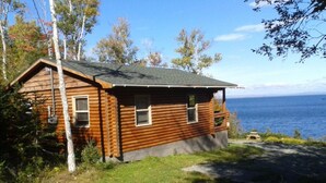 Uma cabana de tronco com varanda, um pequeno deck e vista para o oceano.