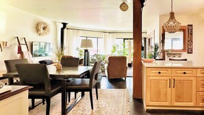 A modern kitchen with wooden cabinets, a dining area with a table and chairs, and a living space with a sofa and plants. - Walk everywhere from Railtown Suite! + spacious, beautiful, & comfortable. (Nelson)