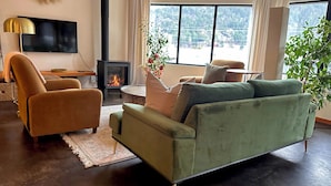 A living room with a sofa, armchairs, a TV, a fireplace, and large windows with a view. - Walk everywhere from Railtown Suite! + spacious, beautiful, & comfortable. (Nelson)