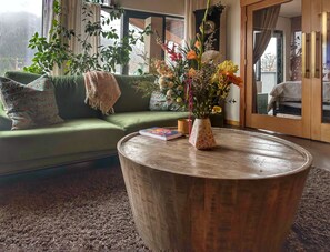 Un salon avec un canapé vert, une table basse ronde en bois et un vase de fleurs.