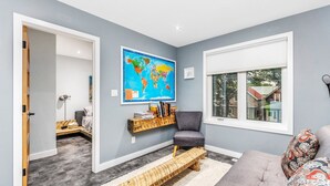 Un salon moderne avec un canapé gris, un banc en bois, une carte du monde accrochée au mur et une fenêtre donnant sur une maison.