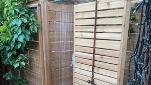 Une douche extérieure en bois, dotée d’un tuyau en métal et d’un banc en bois.