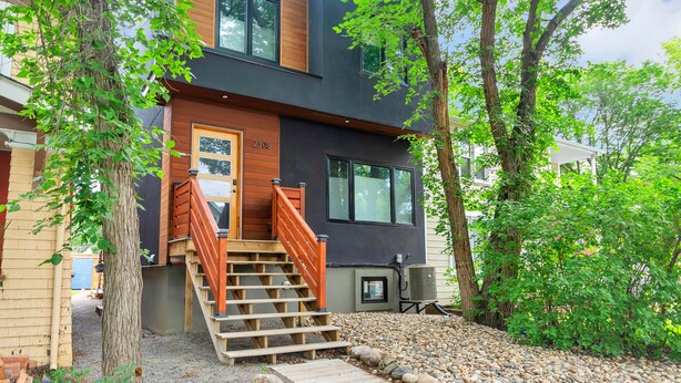 Une maison moderne à deux étages, dotée d’un escalier en bois menant à la porte d’entrée, au numéro 2308, et entourée d’arbres ainsi que d’un chemin de gravier.