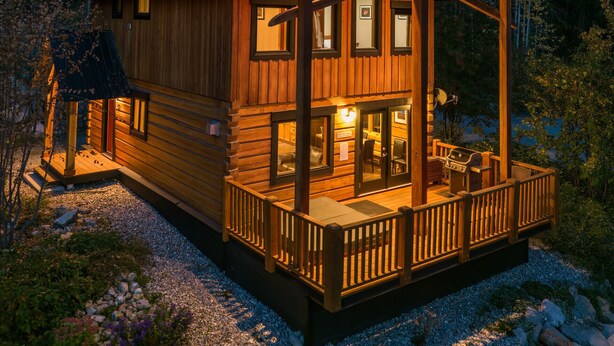 Eine Holzblockhütte mit überdachter Veranda, mehreren Fenstern und Blick auf eine Berglandschaft.