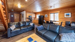 Ein großzügiger Wohnbereich mit zwei schwarzen Ledersofas, einem Holztisch und einer Küche im Hintergrund.