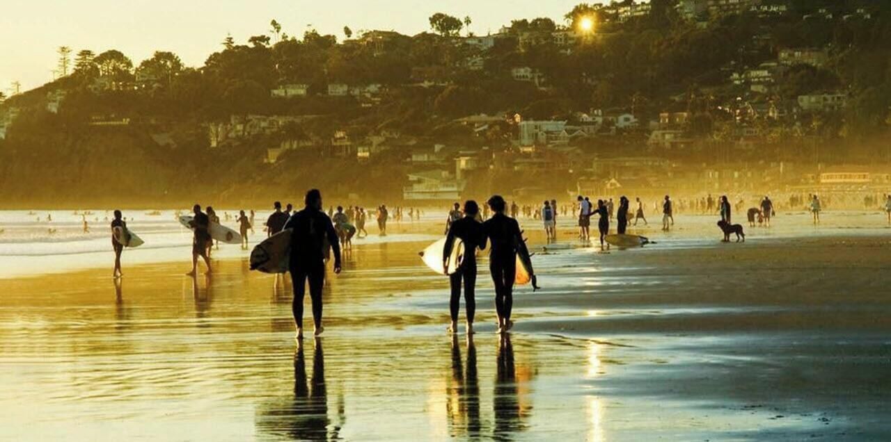 Une scène de plage où l’on voit des personnes se promener et porter des planches de surf, avec un logo et du texte superposés.