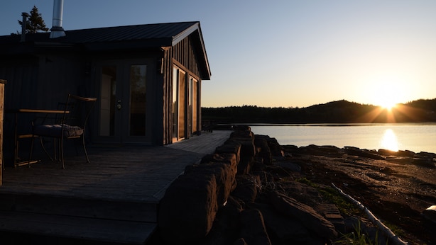 Un chalet au bord du lac, doté d’une terrasse en bois, d’une cheminée et offrant une vue sur le coucher de soleil sur l’eau.