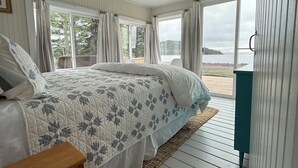 Une chambre avec un grand lit, une table de chevet en bois, une fenêtre avec des rideaux et une vue sur la plage.