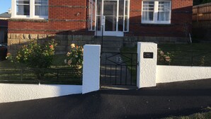 Una casa de ladrillo de dos pisos con fachada blanca, una puerta principal y un pequeño jardín con flores.