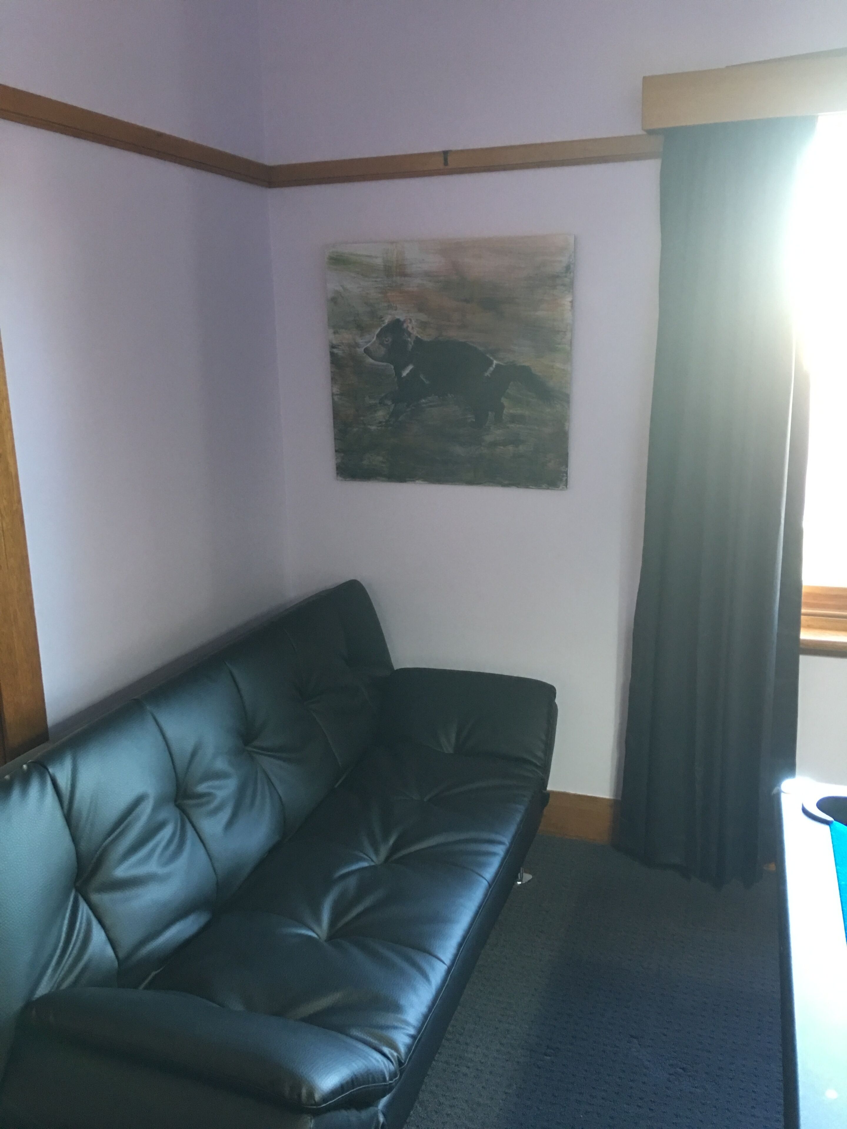 Um quarto com um sofá de couro preto, um quadro na parede e uma janela com cortinas.