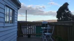 Una terraza de madera con una mesa, sillas, una parrilla y una planta en maceta.