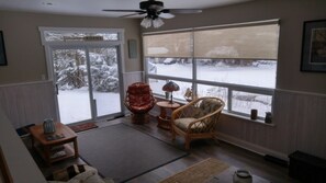 A cozy living room with a large window, a ceiling fan, and a view of a snowy landscape.