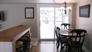 A kitchen with a wooden bar counter, stools, a dining table with chairs, and a chandelier.