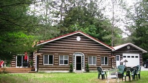 A log cabin with a front porch, a garage, and a small deck area.