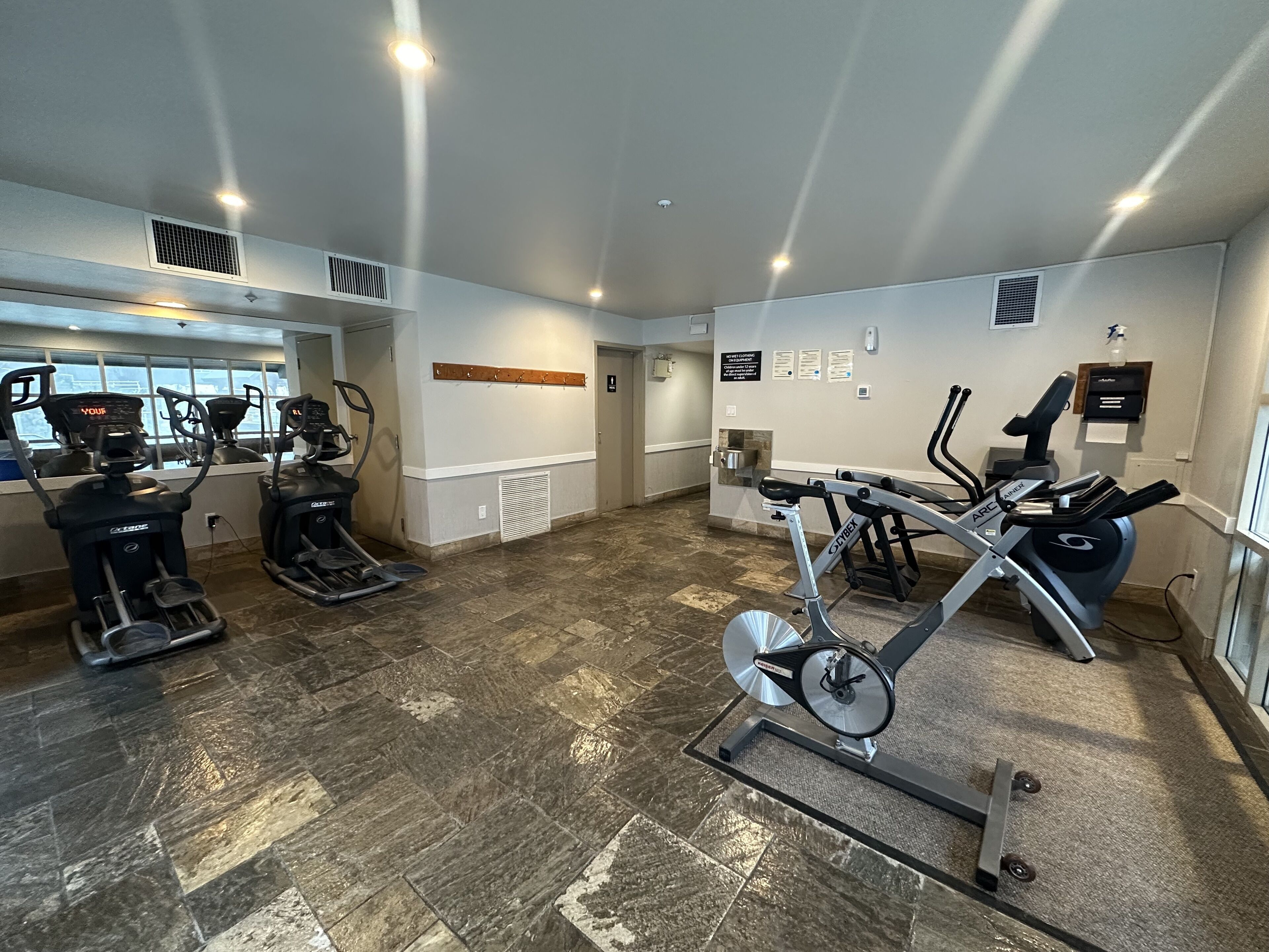 Une salle de sport équipée de tapis de course, de vélos elliptiques et d’un porte-haltères fixé au mur.