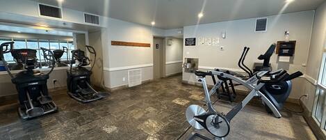 Une salle de sport équipée de tapis de course, de vélos elliptiques et d’un porte-haltères fixé au mur.