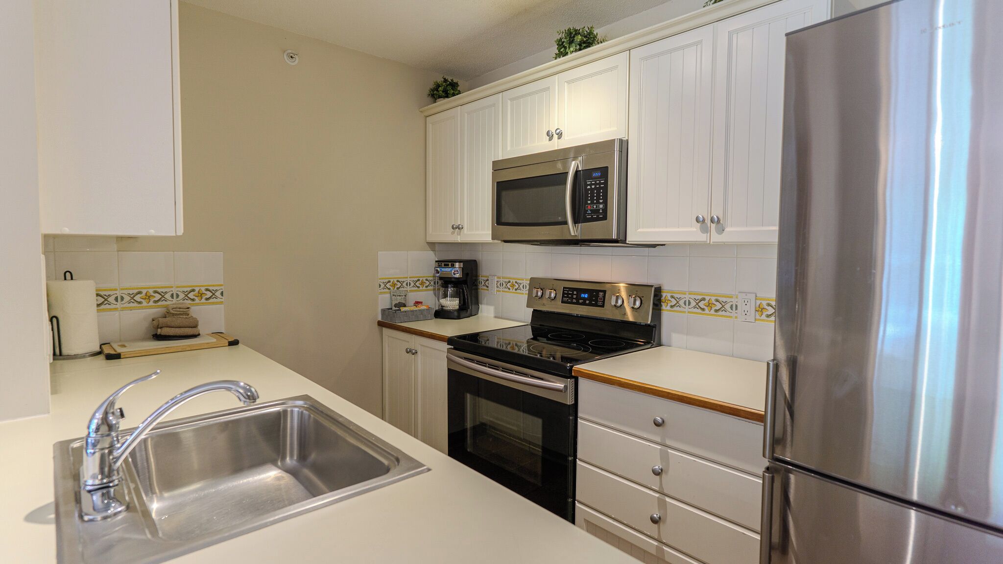 A modern kitchen with stainless steel appliances, white cabinetry, and a tiled backsplash.