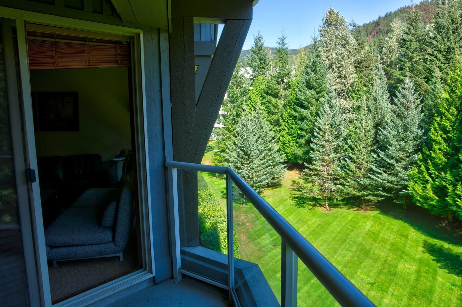A balcony with a view of a well-maintained lawn and dense forest.