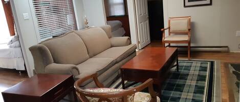 Una sala de estar con un sofá beige, una mesa de centro de madera y un sillón estampado.