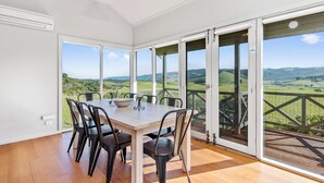 Un comedor con mesa y sillas, ventanas amplias y vistas al campo.