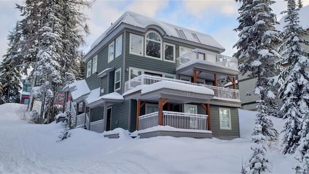 A two-story house with a balcony, surrounded by snow-covered trees.