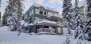 Una casa a due piani con un balcone, circondata da alberi ricoperti di neve.