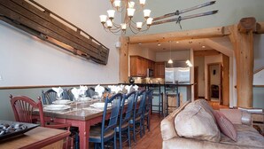 Comedor con una mesa de madera dispuesta para seis personas, sillas azules y una araña.