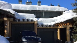 Un edificio con garaje, techo cubierto de nieve y un coche estacionado.