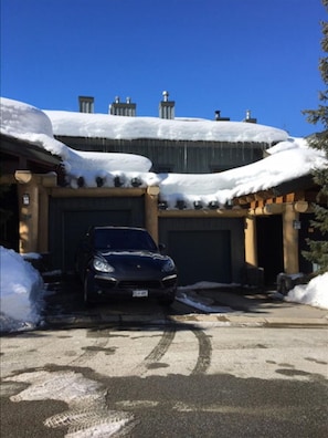 A building with a garage, snow-covered roof, and a parked car. - Luxury 4 Bedroom TRUE Ski in/ ski out Townhome in Exclusive Taluswood (Whistler)