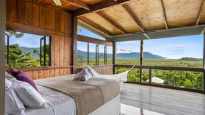 Ein Zimmer aus Holz mit einem Bett, großen Fenstern und Blick auf die Berge.