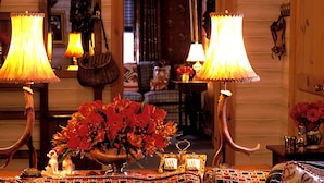Quarto com iluminação acolhedora e decoração em madeira, com um espelho grande, várias luminárias e um arranjo de flores sobre uma mesa.