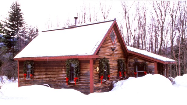 Uma cabana de troncos com telhado coberto de neve, decorada com guirlandas e fitas vermelhas.