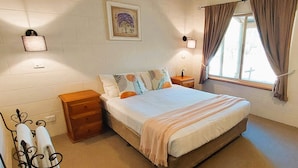 Een slaapkamer met een bed, nachtkastjes, een raam met gordijnen, een wandlamp en een lijst met een afbeelding.