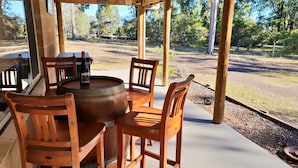 Een overdekt terras met houten stoelen en een ronde tafel, met uitzicht op een natuurlandschap.