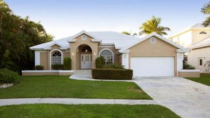 A single-story house with a beige facade, a white garage door, and a well-maintained lawn. - 3/2 Home steps away from Tiger Tail access (Marco Island)